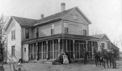 Two story farmhouse with an impressive front porch and the family and horses out front. 